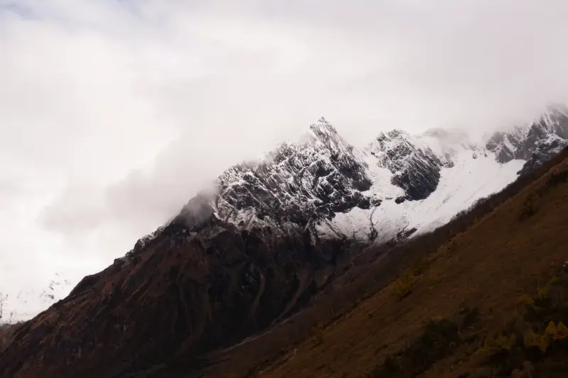 A snow-covered mountain ridge rising above a dark foreground slope.