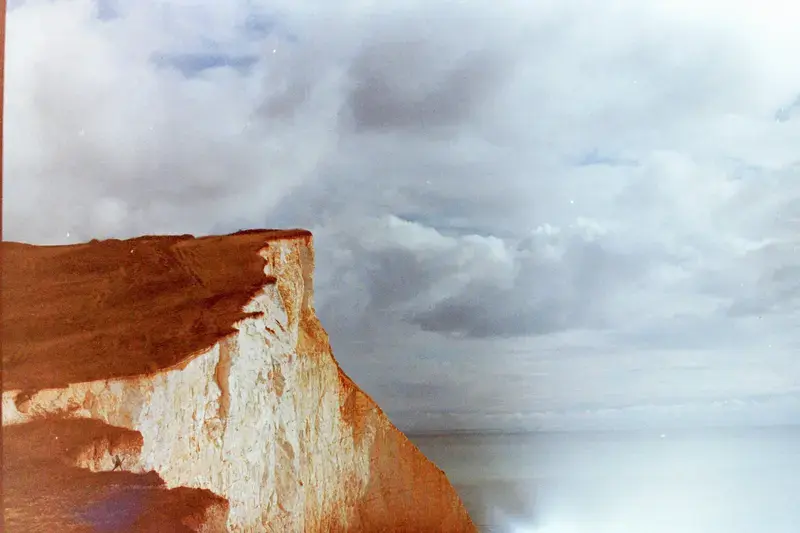 A pale red cliff meeting dark clouds and a bright patch of sky.