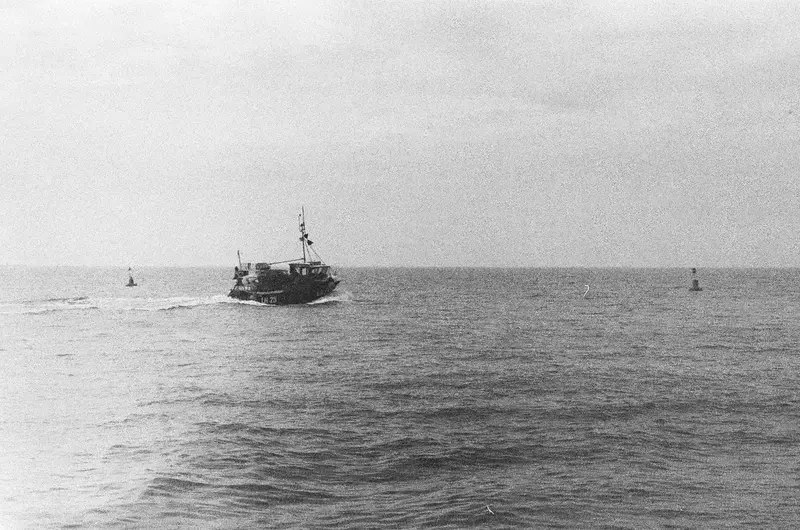 A small fishing boat on a calm black-and-white sea.